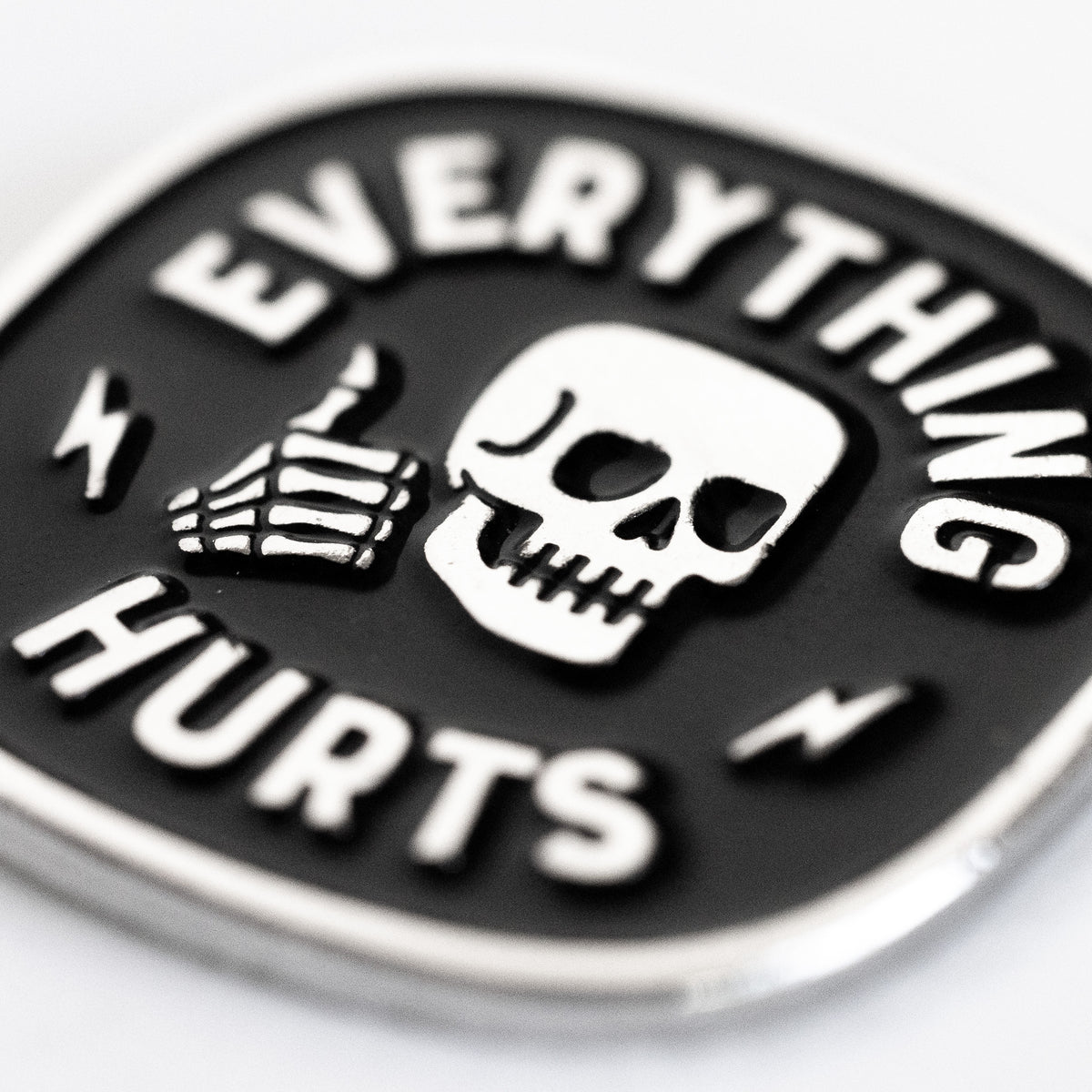 A close macro view shows the Everything Hurts enamel pin, its grinning skull and bony thumbs up catching the light.