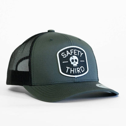 Angled on white, the charcoal Safety Third trucker hat shows its skull patch and black mesh side panels.