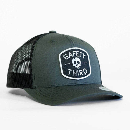 Angled on white, the charcoal Safety Third trucker hat shows its skull patch and black mesh side panels.