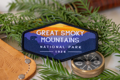 Set on fir branches beside a brass compass, the Great Smoky Mountains patch shows its orange sky and lettering.
