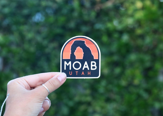 Farther back against the same hedge, the Moab Utah sticker shows its arched shape and white lettering.
