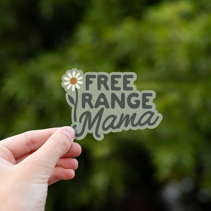 Close and centered, the Free Range Mama sticker rests in a hand with green leaves blurred behind it.
