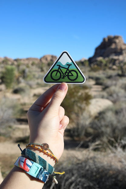 Raised toward blue desert sky, the green mountain bike sticker stands out over boulders and scrub.