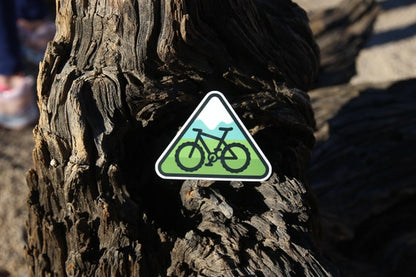 Pressed onto a cracked driftwood trunk, the mountain bike trail sticker catches full sun.