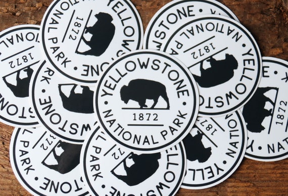 Scattered across weathered wood, a pile of Yellowstone National Park B&W stickers overlaps face up.