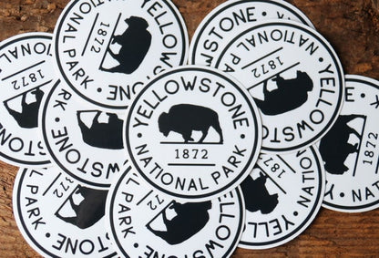 Scattered across weathered wood, a pile of Yellowstone National Park B&W stickers overlaps face up.