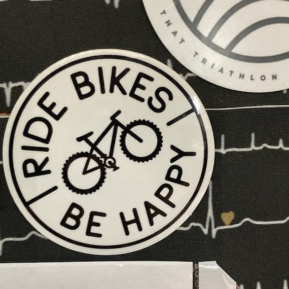 Stuck to a black notebook printed with heartbeat lines, the Ride Bikes Be Happy sticker sits beside another decal.