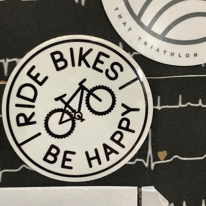 Stuck to a black notebook printed with heartbeat lines, the Ride Bikes Be Happy sticker sits beside another decal.