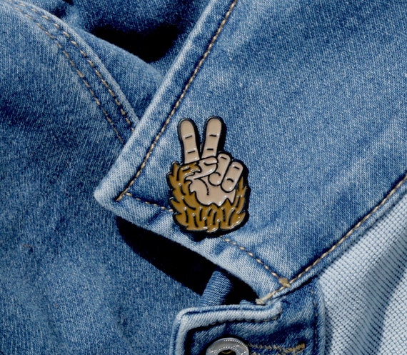 Fastened through the collar of a faded denim jacket, the Bigfoot Peace Pin catches the stitching lines.