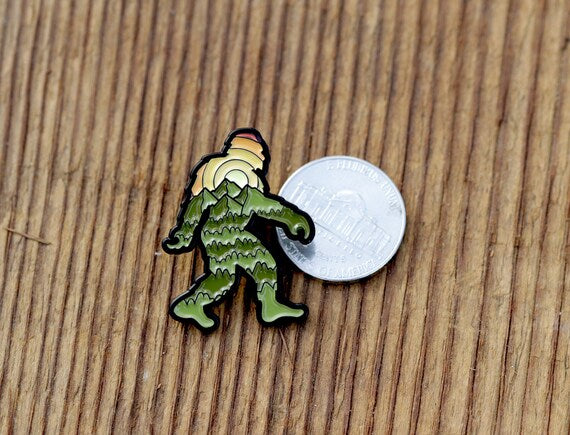 Squared to the camera on planks, the Bigfoot Adventure Pin sits next to a nickel showing how small it is.