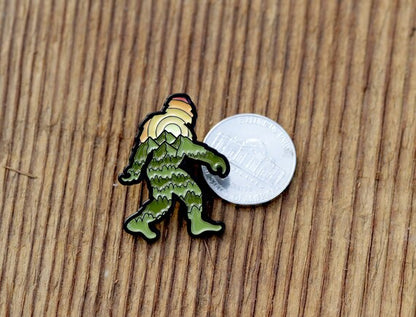 Squared to the camera on planks, the Bigfoot Adventure Pin sits next to a nickel showing how small it is.