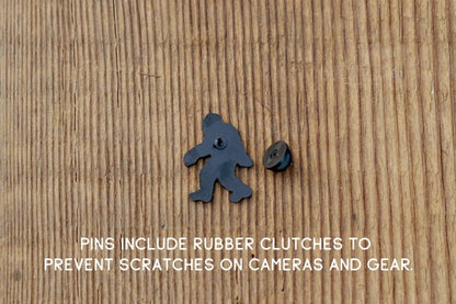 Back side of the Bigfoot Adventure Pin lies on wood with its rubber clutch and a note about scratches.