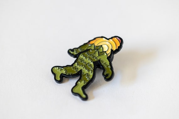 Turned on its side against white, the Bigfoot Adventure Pin catches light along the black outline.