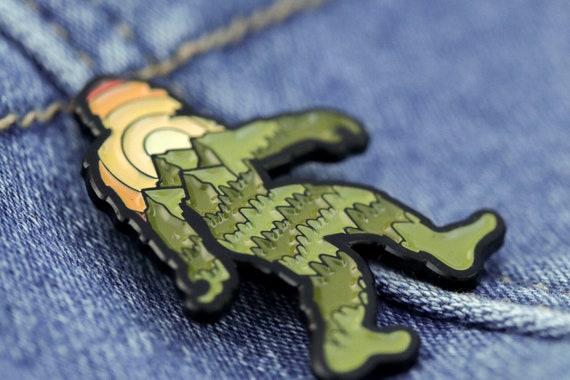 Pinned to blue denim near the stitching, the Bigfoot Adventure Pin fills the frame in close focus.