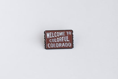 Straight on and centered, the Welcome to Colorful Colorado pin reads clearly against a pale background.
