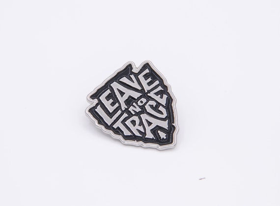 Straight on and centered, the Leave No Trace enamel pin sits flat with crisp white letters on black.