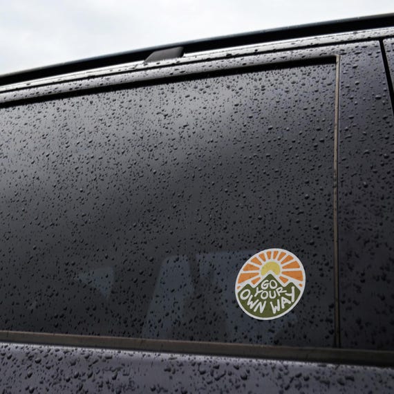 Stuck to a rain covered black car window, the Go Your Own Way sticker sits below the beltline.