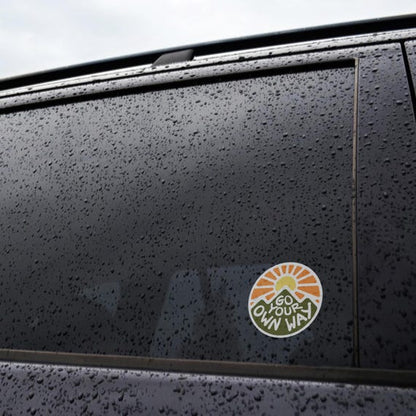Stuck to a rain covered black car window, the Go Your Own Way sticker sits below the beltline.