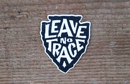Stuck flat on rough brown bark, the Leave No Trace sticker shows its black arrowhead and small pine tree.