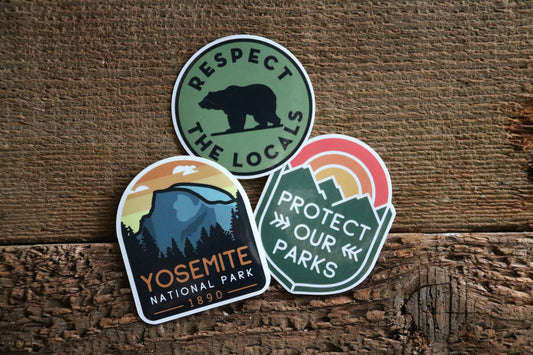 Three stickers lean on weathered wood, with the Yosemite National Park sticker beside bear and parks designs.