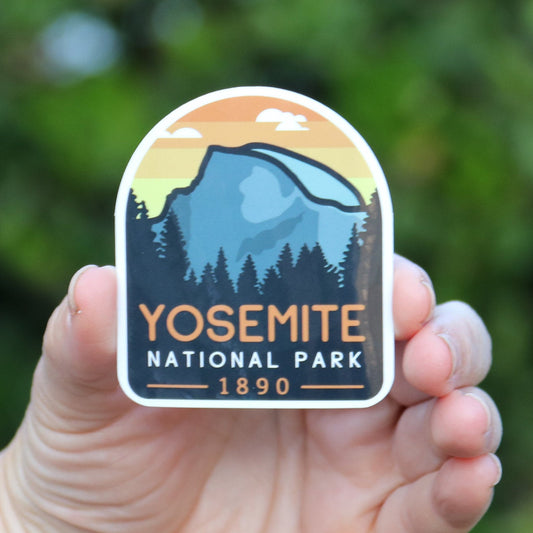 Held at arm's length, the Yosemite National Park sticker sits small against deep green leaves.