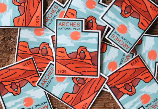 Scattered across weathered wood, a pile of Arches National Park stickers overlaps at every angle.