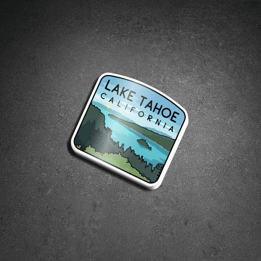 Resting on grey textured stone, the Lake Tahoe sticker tilts to one side and casts a soft shadow.