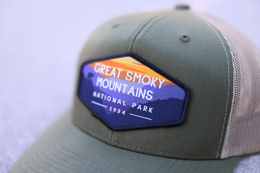 Stitched to the front of an olive trucker hat, the Great Smoky Mountains patch sits beside tan mesh.